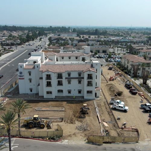 The image shows a construction site with buildings, vehicles, and equipment. The surrounding area has residential and commercial structures.