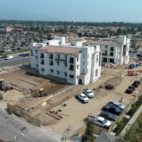 Aerial view of a construction site with a building in progress, surrounded by cars and equipment, in a suburban area.