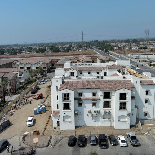 Aerial view of a multi-story building with a parking lot, surrounded by residential areas and roads in the background.