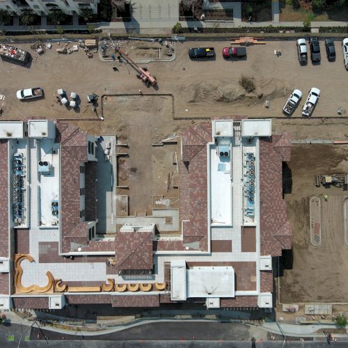 Aerial view of a large construction site with a building under development, surrounded by parked cars and construction equipment.