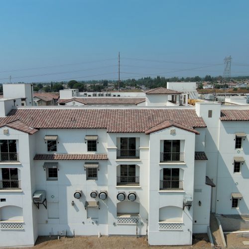 A white multi-story building with a red-tiled roof, surrounded by a construction site and roads, under a clear blue sky.