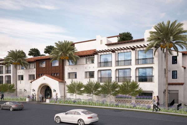 A modern three-story building with arched entrance, palm trees, and parked cars on the street, likely a residential or commercial property.