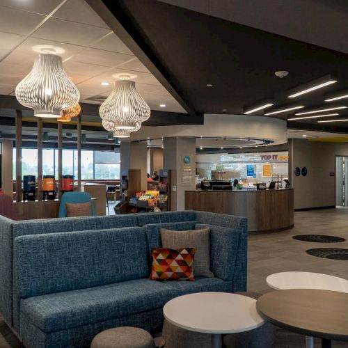 This image shows a modern lounge area with a blue sofa, round tables, decorative lights, and a counter in the background.