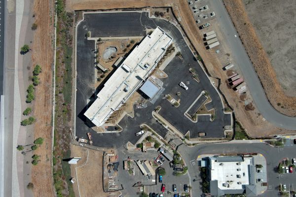 An aerial view of a construction site with a large building, surrounded by roads and parked cars.