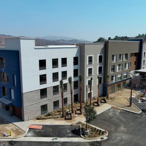 A modern, multi-story building under construction with a partially developed surrounding landscape is shown in the image.