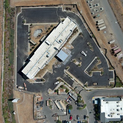 An aerial view of a construction site with a large building, surrounding roads, and parking areas.