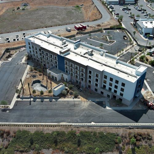 An aerial view of a large building surrounded by a mostly paved area, with nearby roads and scarce green patches in the vicinity.