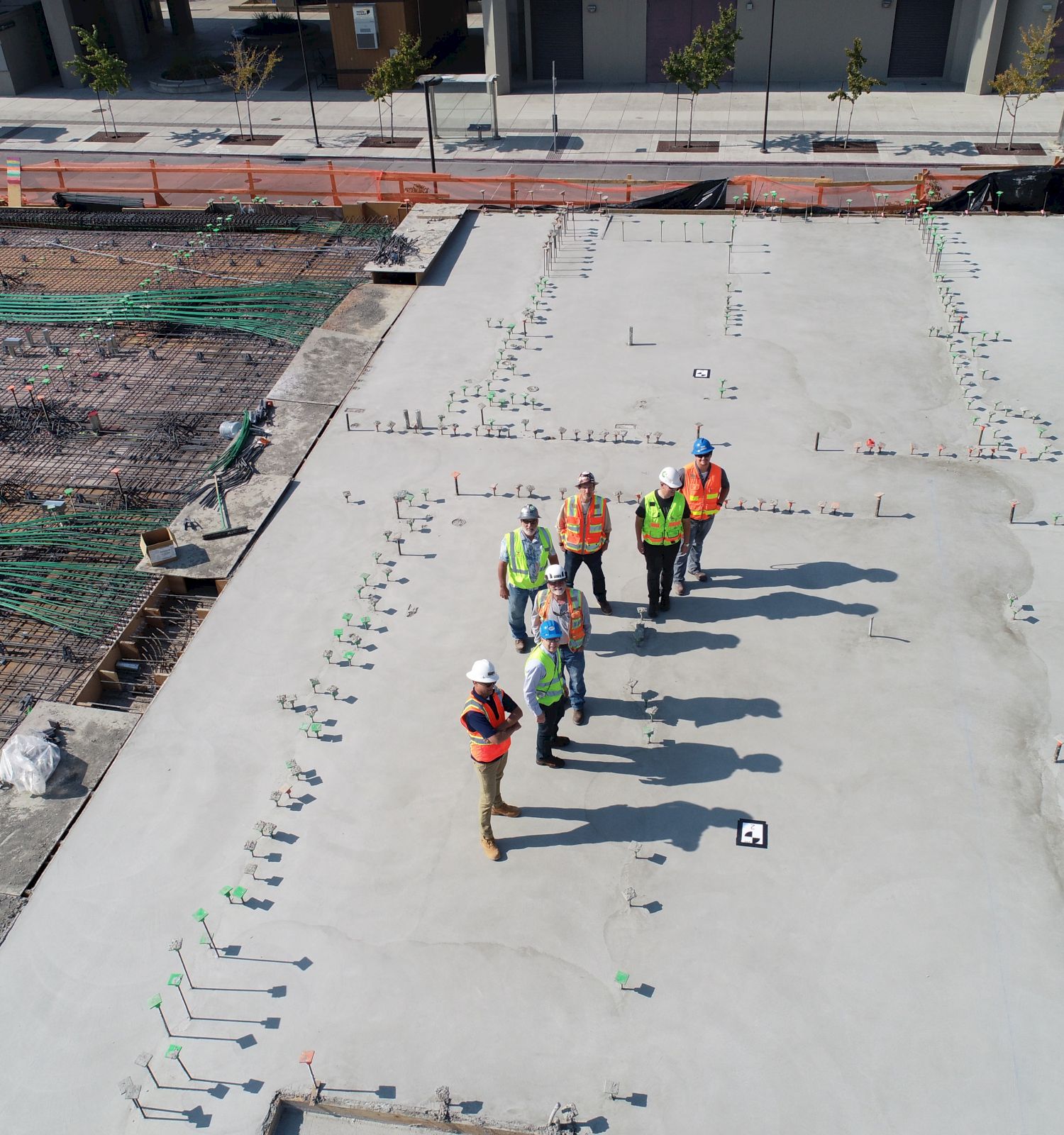 A group of people in construction attire stands on a partially completed concrete structure, observed from an aerial perspective, during daylight.